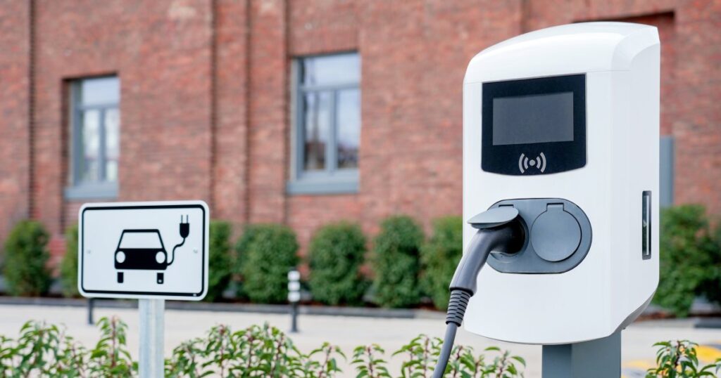 witte laadpaal met bord en kabel met rode muur in achtergrond